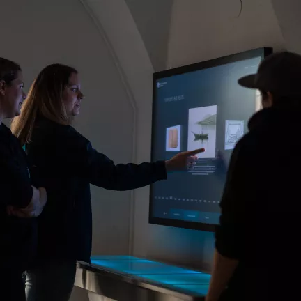 touchscreen auf der wand. drei menschen darum herum.