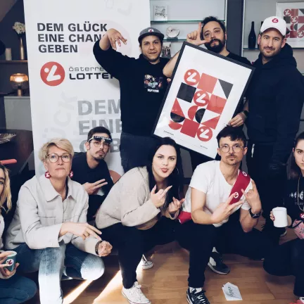 Die Crew der Werbefilmproduktion steht vor einem Banner der österreichischen Lotterien und schaut ernst in die Kamera. Es sind neun Personen.