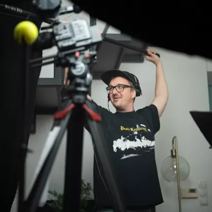 Tontechniker mit einer Boom in der Hand. Er lächelt.
